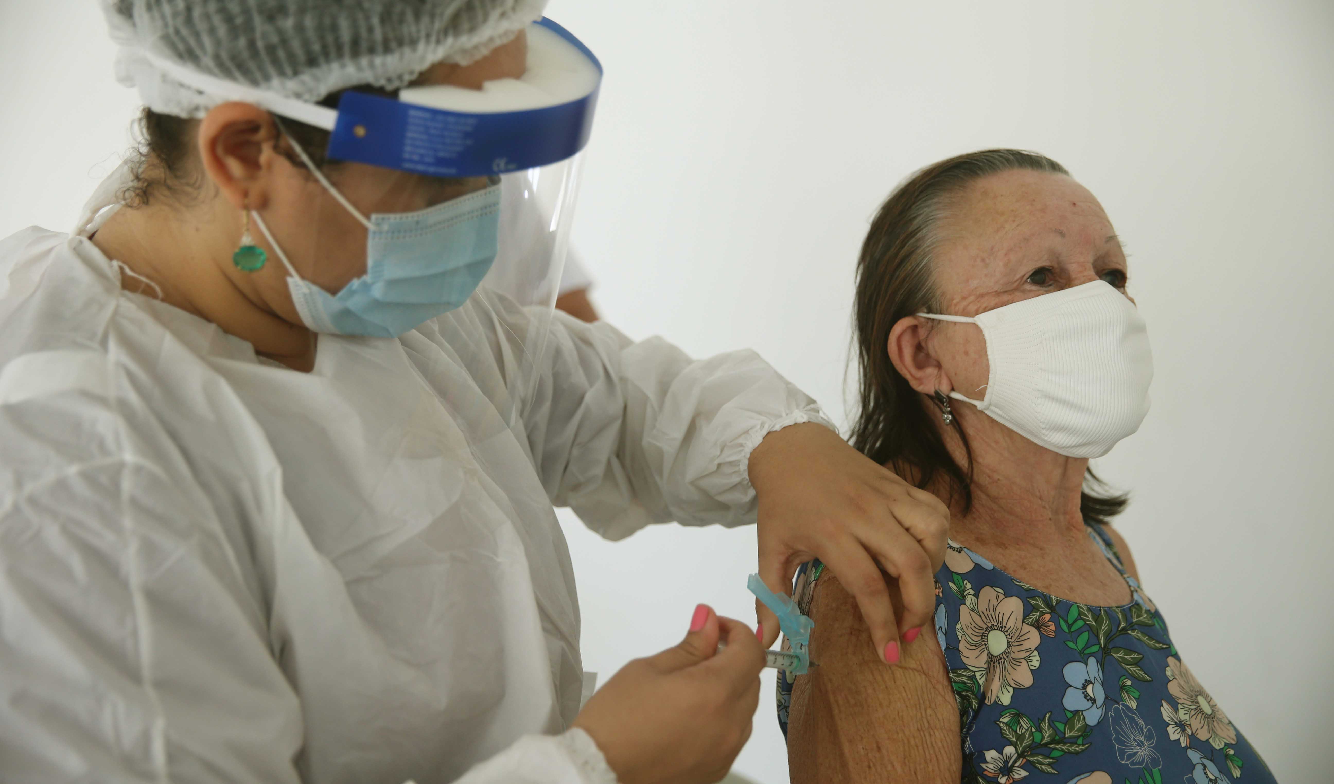 senhora de máscara sendo vacinada